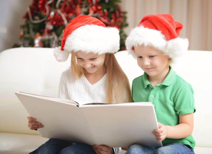 2 Kinder mit Weihnachtsmützen lesen in einem Buch