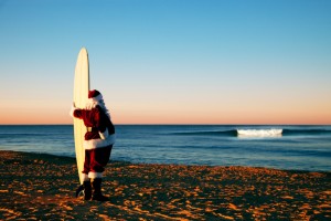 Weihnachtsmann mit Surfbrett am Strand